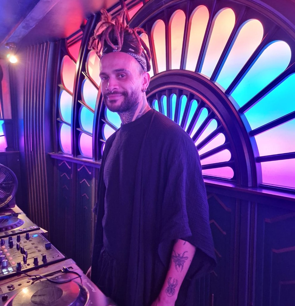 Facilitator standing by a DJ booth in front of a colourful lit archway